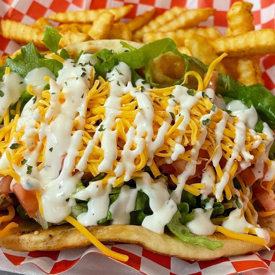 A close-up of a taco with lettuce, tomatoes, shredded cheese, and white sauce, served with fries.