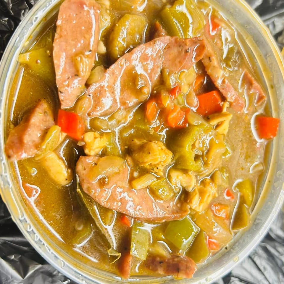 Hearty American gumbo with sausage, chicken, okra, and peppers in a clear takeout container.