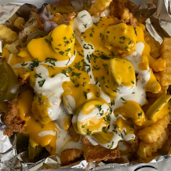 Loaded fries with melted cheese, white sauce, and green herbs in a foil container.