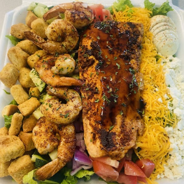 Grilled salmon and shrimp salad with croutons, cheese, and sliced egg in a white takeout container.